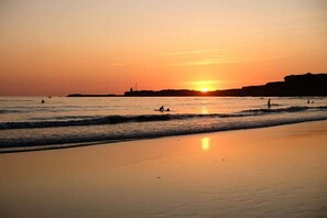 Ein Strand mit Wellen, einem Sonnenuntergang und stilisierte Menschenbilder.