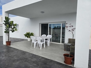 A modern outdoor patio with a table and chairs, potted plants, and a sliding glass door. - Beautiful New House with a Private Pool (Conil De La Frontera)