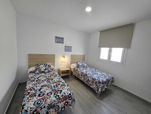 A room with two beds, a nightstand, a wall-mounted light, and a window with a blind. - Beautiful New House with a Private Pool (Conil De La Frontera)