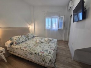 Ein Schlafzimmer mit Bett, Nachttisch, Wand-Fernseher und einem Fenster mit Vorhängen.