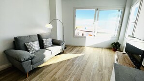 Ein modernes Wohnzimmer mit einem grauen Sofa, einer Stehlampe und einem großen Fenster mit Blick auf die Stadt.