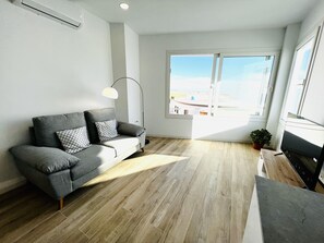 Ein modernes Wohnzimmer mit einem grauen Sofa, einer Stehlampe und einem großen Fenster mit Blick auf die Stadt.