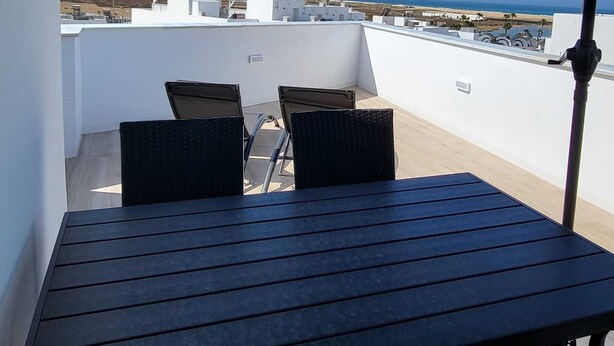 Ein Balkon mit Tisch und Stühlen, der auf eine Küstenlandschaft mit Gebäuden und einem Strand blickt.