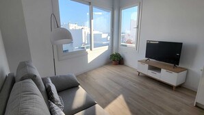 Ein modernes Wohnzimmer mit Sofa, Fernseher und großen Fenstern.