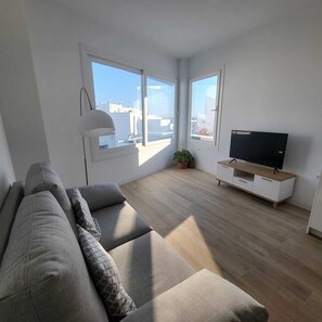 Ein modernes Wohnzimmer mit Sofa, Fernseher und großen Fenstern.