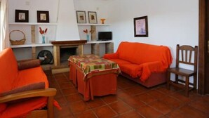 A living room with two orange sofas, a wooden chair, a small table with a colorful tablecloth, a fireplace, and a TV on a stand. - P1 - With pool and garden, minutes from the sea. (Conil De La Frontera)