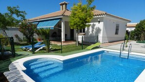A swimming pool with a white edge, a covered patio, and a white building with a tiled roof. - P1 - With pool and garden, minutes from the sea. (Conil De La Frontera)