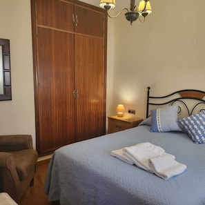 Ein Schlafzimmer mit Bett, Kissen, Nachttisch, Lampe, Kleiderschrank und einem Sessel.
