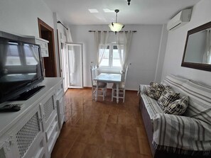 Ein Wohnzimmer mit Fernseher, Esstisch und einer Couch.