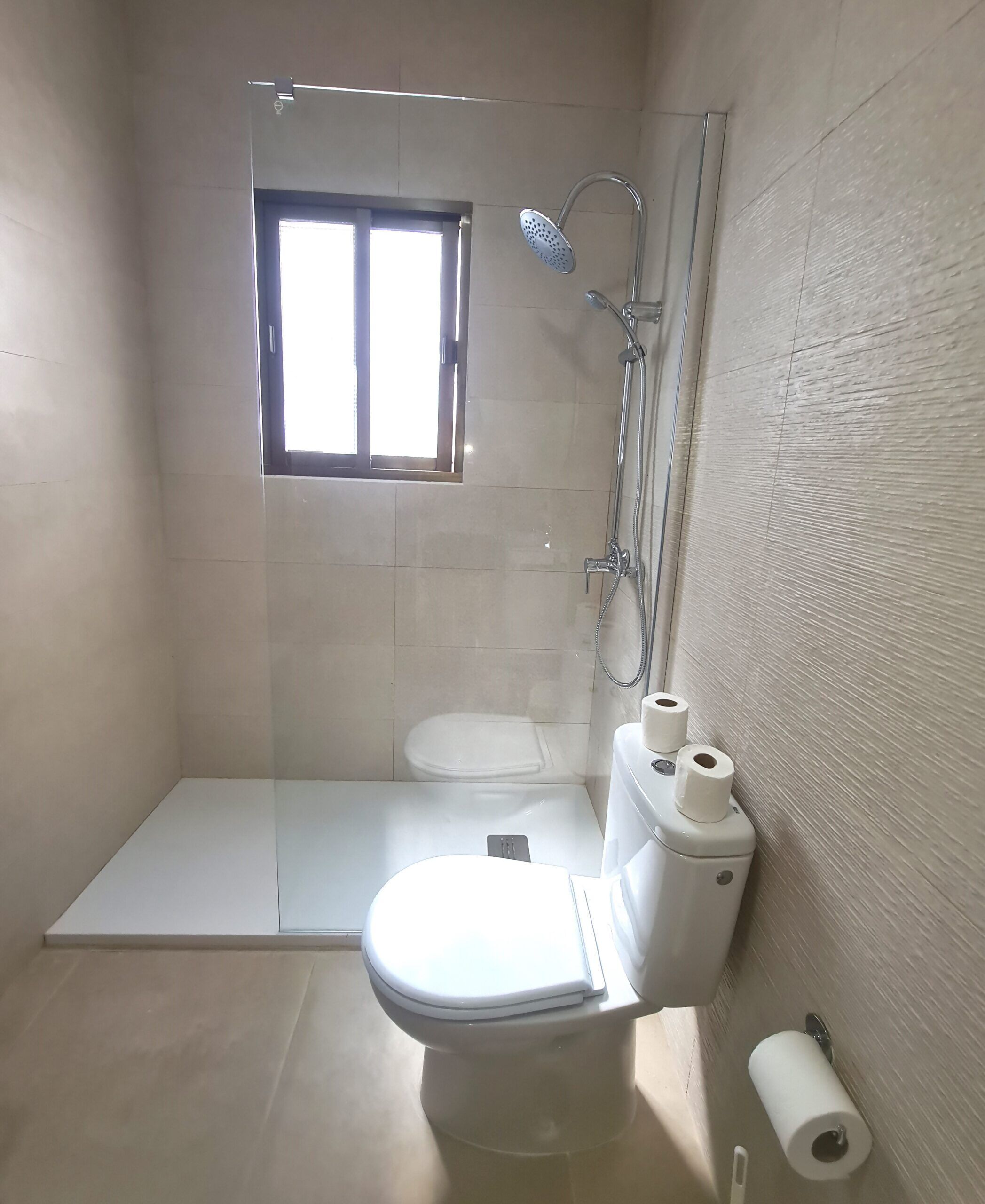 Ein Badezimmer mit Dusche, Toilette und einem Fenster.