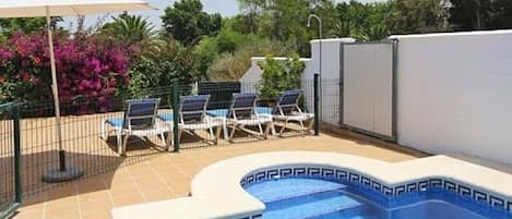 A swimming pool with a blue border, surrounded by a fence, and a few lounge chairs.