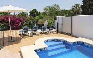 Ein Swimmingpool mit blauer Umrandung, umgeben von einem Zaun und einigen Liegestühlen.