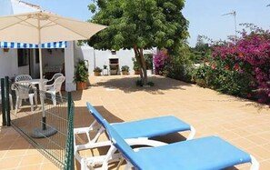 Eine Terrasse mit Tisch und Stühlen, ein überdachter Sitzbereich und ein Baum.
