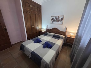 A bedroom with a bed, a wardrobe, a nightstand, a lamp, and a wall art piece. - Coquettish house with private area near the sea (Conil De La Frontera)