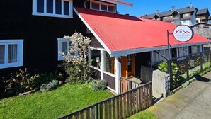 A two-story building with a red roof, a visible sign with a mountain logo, and a well-maintained lawn. - Hotel Casa Ellies Boutique (Puerto Varas)