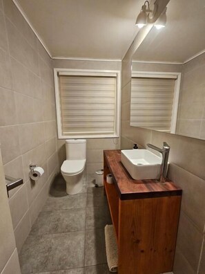 A bathroom with a toilet, sink, and two windows with blinds. - Hotel Casa Ellies Boutique (Puerto Varas)