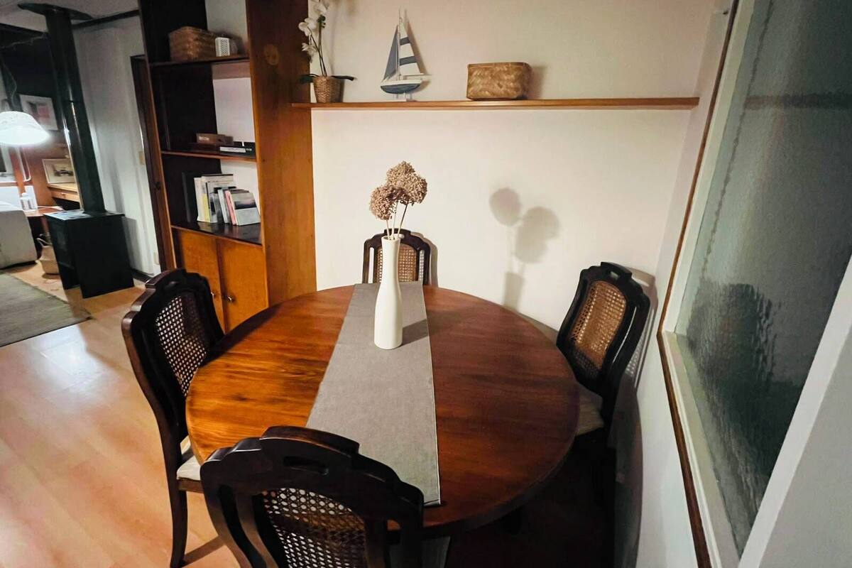 Una mesa redonda de comedor con un jarrón de flores secas, rodeada de sillas.