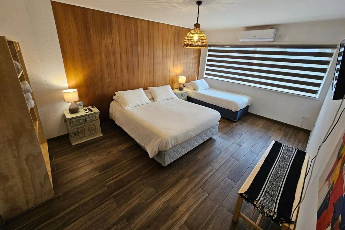 Un dormitorio con dos camas, una pared de madera, una lámpara colgante, una ventana con persianas y un banco.