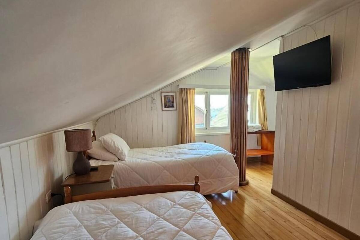 Una habitación con dos camas, un televisor montado en la pared y una ventana con cortinas.