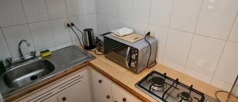 Una cocina compacta con armarios blancos, una estufa a gas, un tostador y un lavamanos.