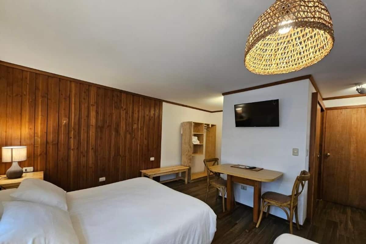 Habitación de hotel con dos camas, un escritorio, una silla, un televisor y una pared de madera.