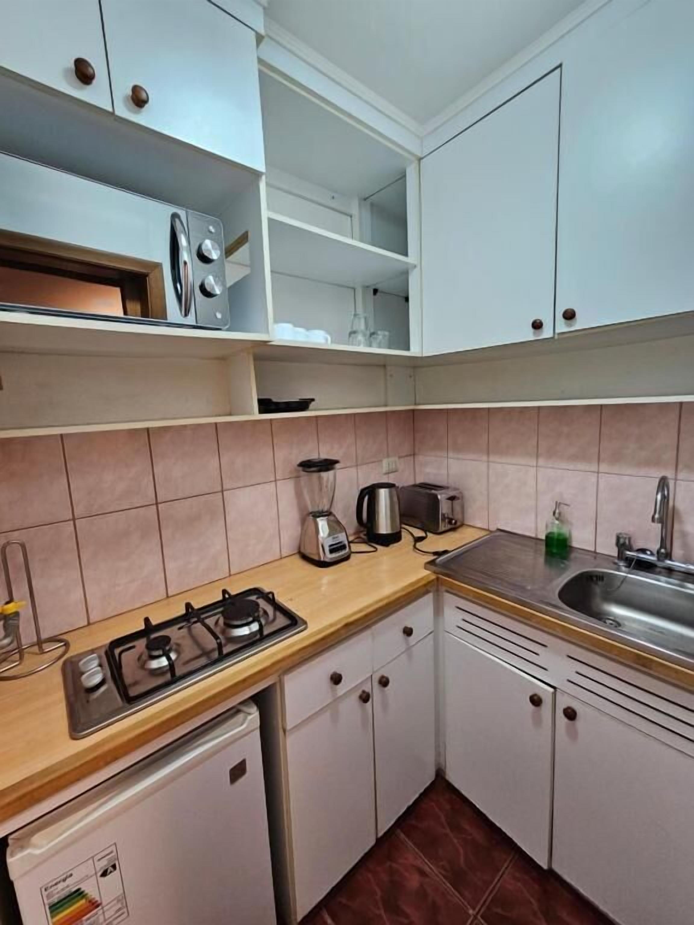 A compact kitchen with white cabinets, a gas stove, a sink, and a small refrigerator.