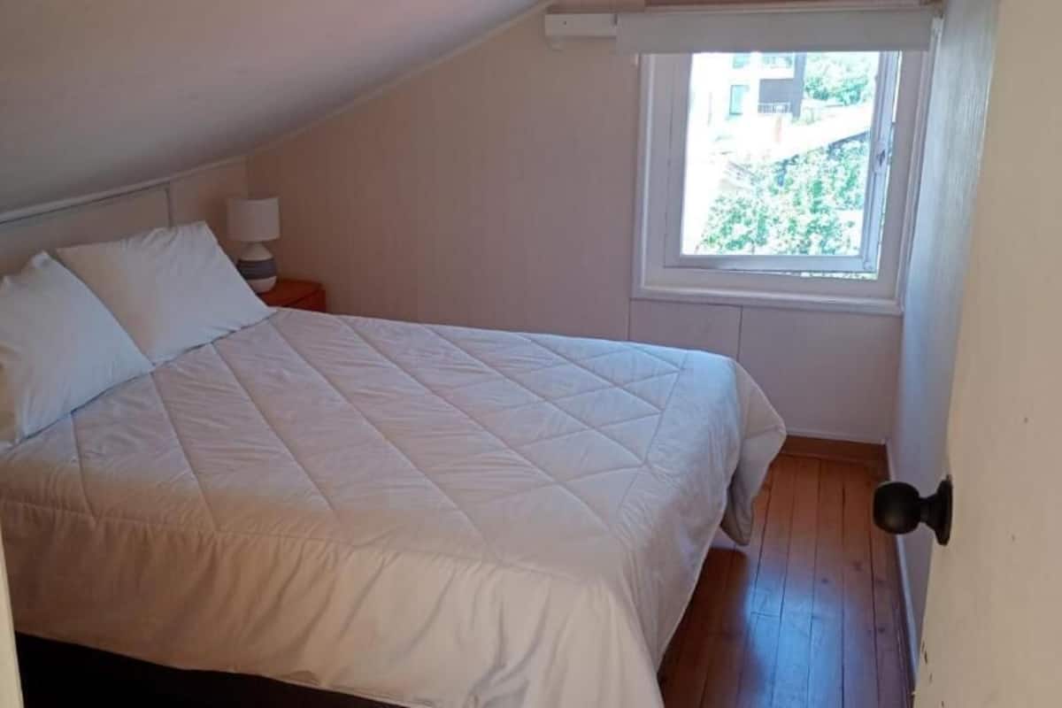 Un dormitorio con cama, mesita de noche, ventana y puerta.