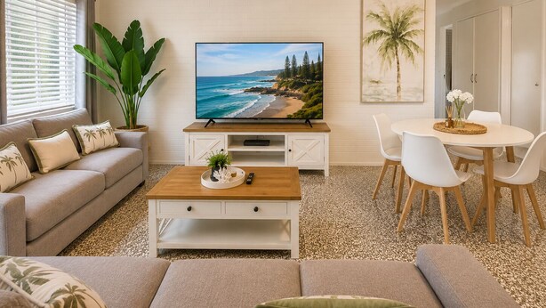 Sala de estar com televisão, sofá, mesa de centro e espaço de jantar.