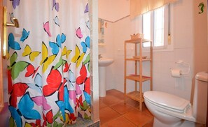 Et badeværelse med toilet, en hylde, et bruseforhæng med sommerfuglemønster og et vindue.