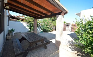 A covered patio with a wooden table and benches, a brick pillar, and a white building with a tiled roof. - Vrbo Property (Conil De La Frontera)