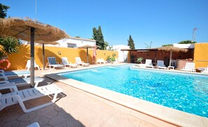 A swimming pool with lounge chairs and a thatched umbrella. - Vrbo Property (Conil De La Frontera)