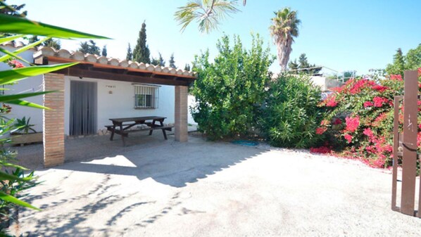 A patio area with a table and chairs, surrounded by greenery and a building with a tiled roof. - Vrbo Property (Conil De La Frontera)