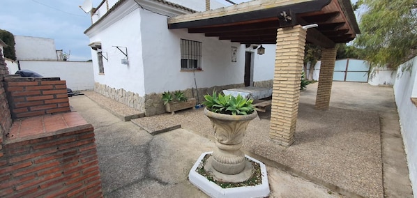 A courtyard with a white building, a stone planter with plants, a brick wall, and a pergola. - Samuel house with community pool and porch (Conil De La Frontera)