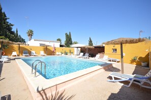 A swimming pool with lounge chairs and umbrellas, surrounded by yellow walls and palm trees. - Samuel house with community pool and porch (Conil De La Frontera)