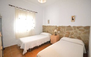 A bedroom with two beds, a window with curtains, a stone wall, and a small bedside table with a lamp. - Samuel house with community pool and porch (Conil De La Frontera)