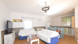 Een kamer met twee bedden, een televisie, een tafeltje, een kroonluchter en een keukenhoek.