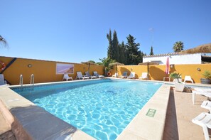 A swimming pool with lounge chairs and a lifebuoy, surrounded by a yellow wall and palm trees. - Samuel house with community pool and porch (Conil De La Frontera)