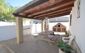 Eine Terrasse im Freien mit einem Holztisch, Bänken, einem Grill aus Ziegelsteinen und einem Blumentopf.