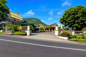 A hotel entrance with a paved driveway leading to the main building, surrounded by greenery and a mountain backdrop.
