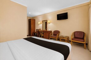 A hotel room with a large bed, a desk, two chairs, a television, and a mirror.