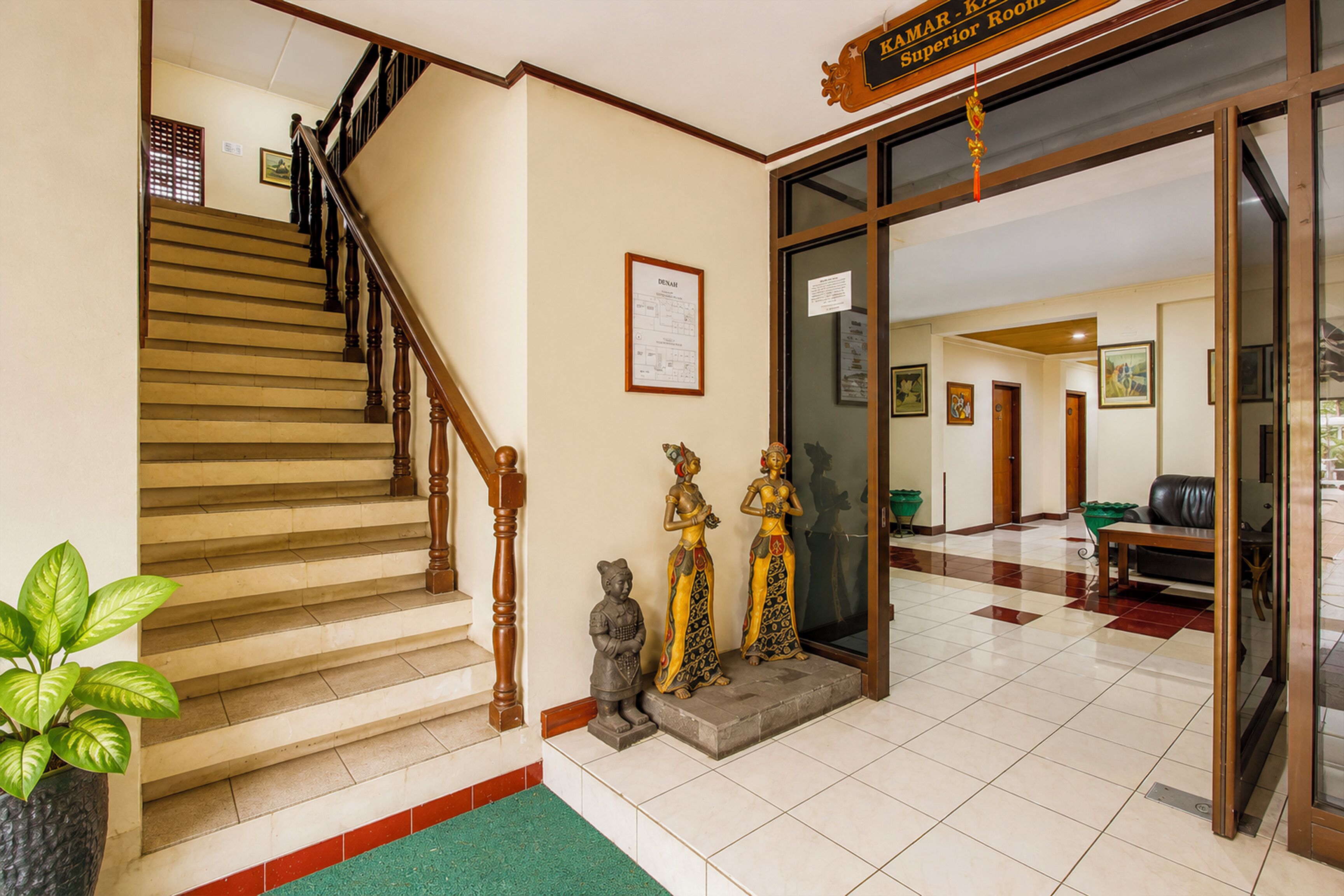 Un vestíbulo de hotel con una escalera, una recepción y un cartel que dice 'KAMAR - Habitación Superior'.