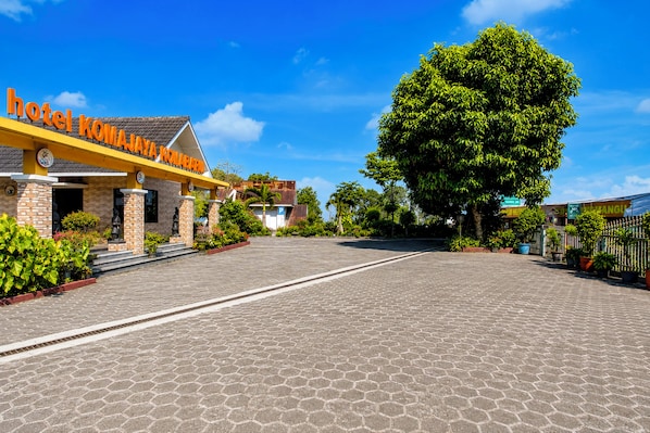 A hotel entrance with a paved driveway, a large tree, and a signboard.