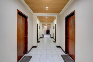 Pasillo de hotel con puertas de madera, suelo de baldosas blancas y techo de madera.