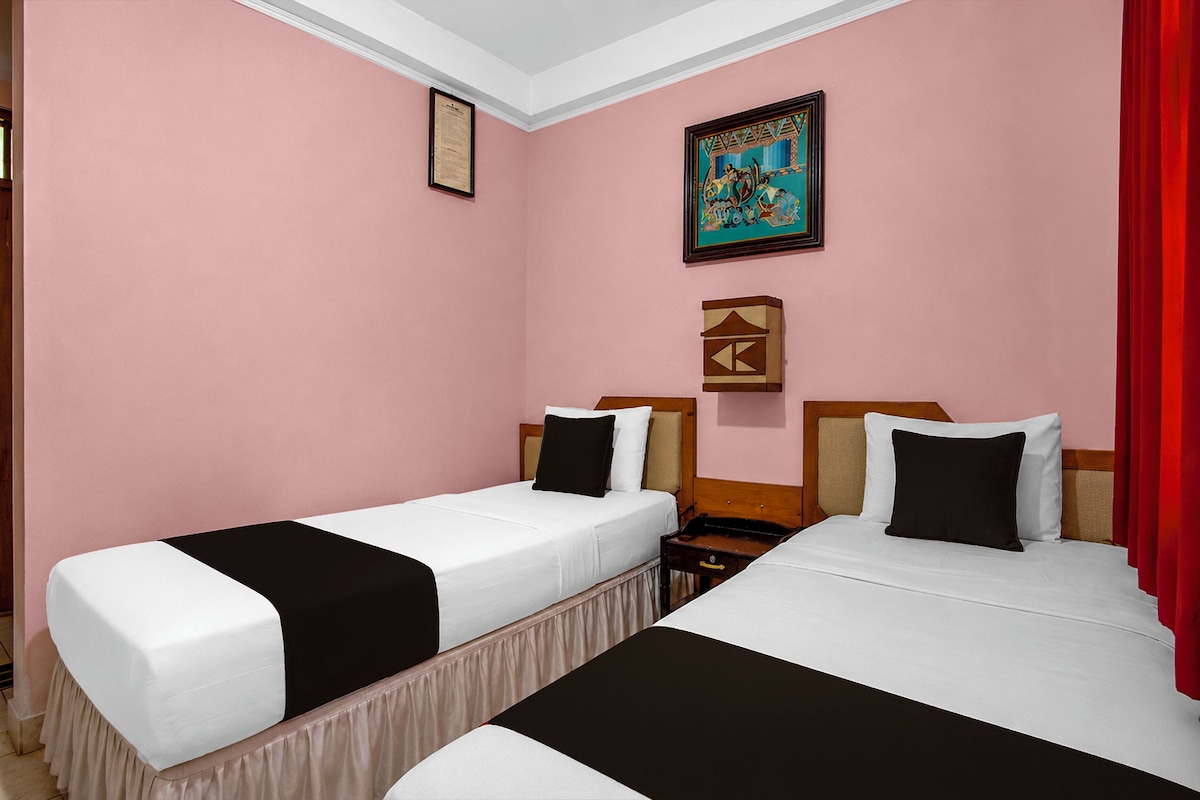 A hotel room with two beds, a nightstand, a framed picture, and a red curtain.
