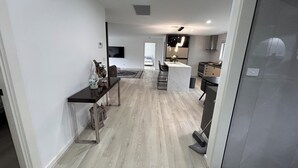 A modern kitchen with a marble island, a dining area with a black table and chairs, and a living room with a TV. - Beautiful 4 bedroom for short or long term stay! (Hastings)