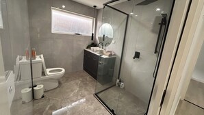 A modern bathroom with a glass shower enclosure, a toilet, and a sink with a mirror above. - Beautiful 4 bedroom for short or long term stay! (Hastings)