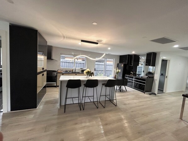 A modern kitchen with a central island, bar stools, and a dining area.