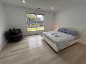 A bedroom with a bed, a sofa, a window, and a hanging light fixture.
