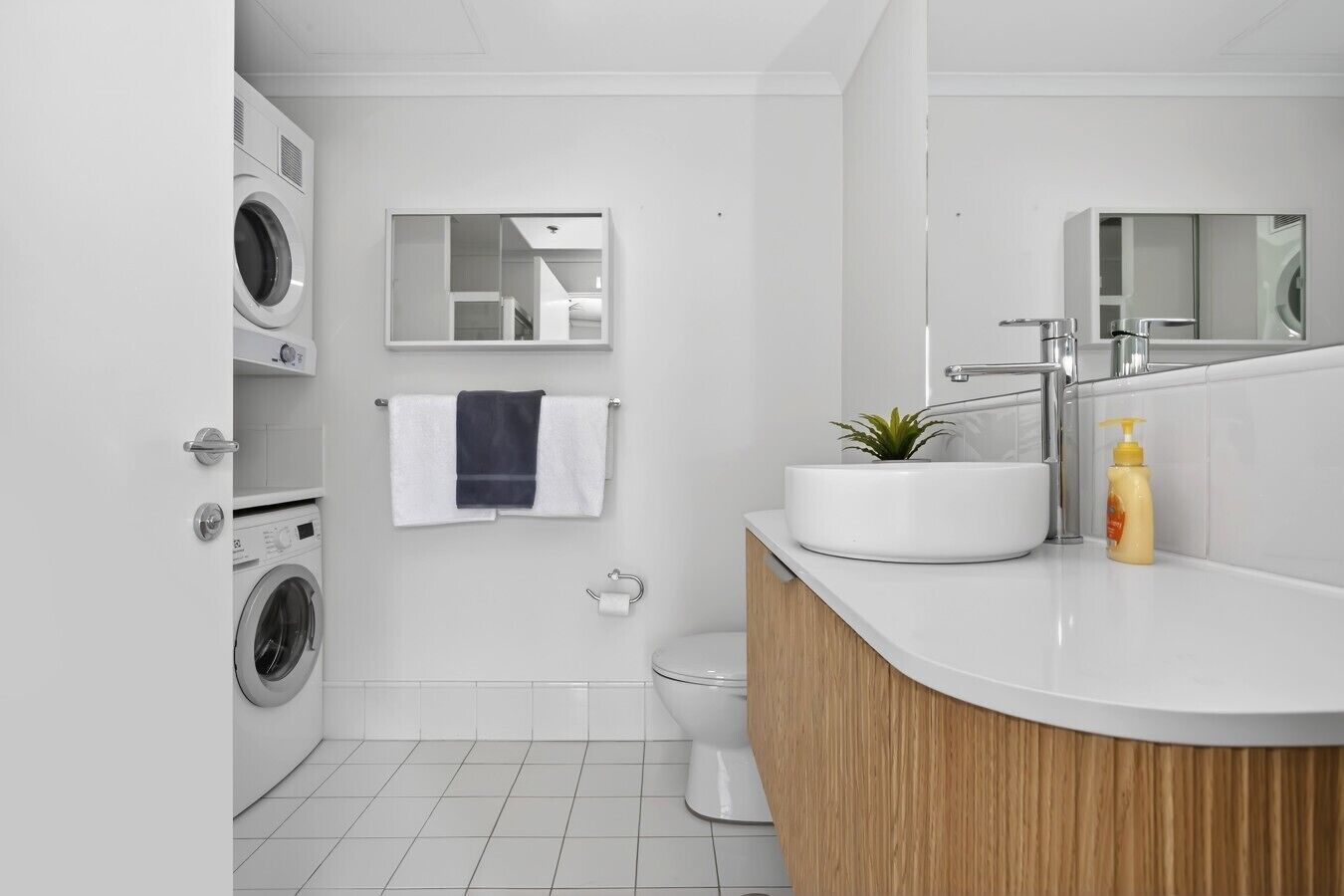 A modern bathroom with a built-in washing machine, a sink with a mirror, and a toilet.