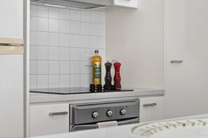 Eine Küche mit weißen Schränken, einem Edelstahlbackofen und zwei Pfeffermühlen auf der Arbeitsplatte.